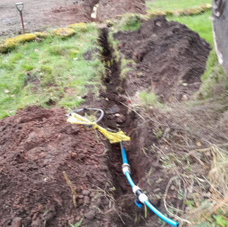 a long slim channel dug into a garden with blue plumbing pipework on view