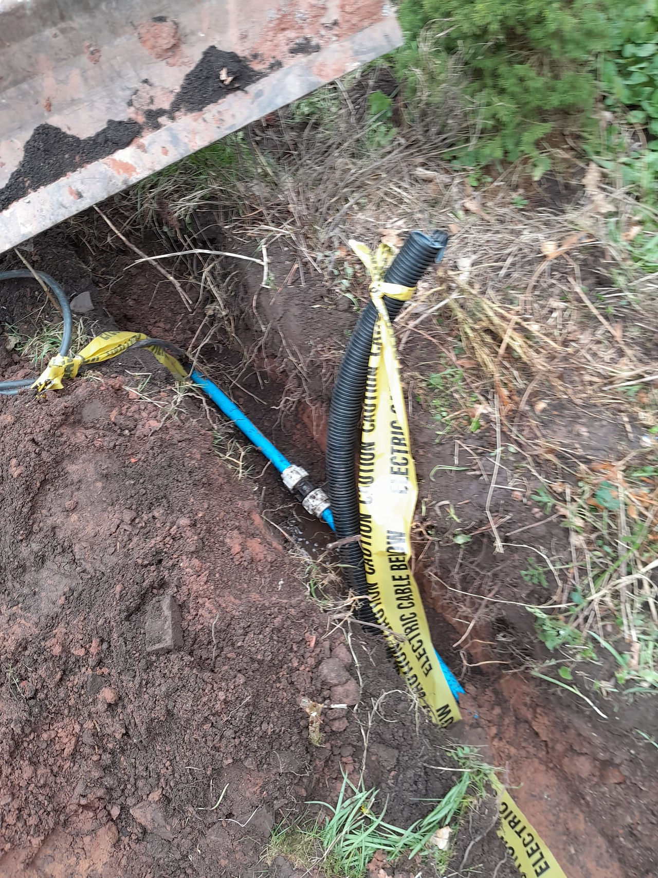 a dug out channel in a garden with blue pipework and yellow construction tape