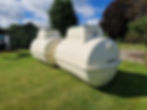 two big cream septic tanks sitting one behind each other on a lawn