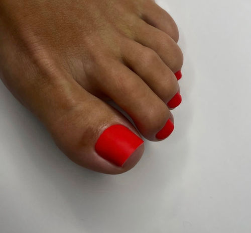 Close up of foot with bright red matte toenails on white background.