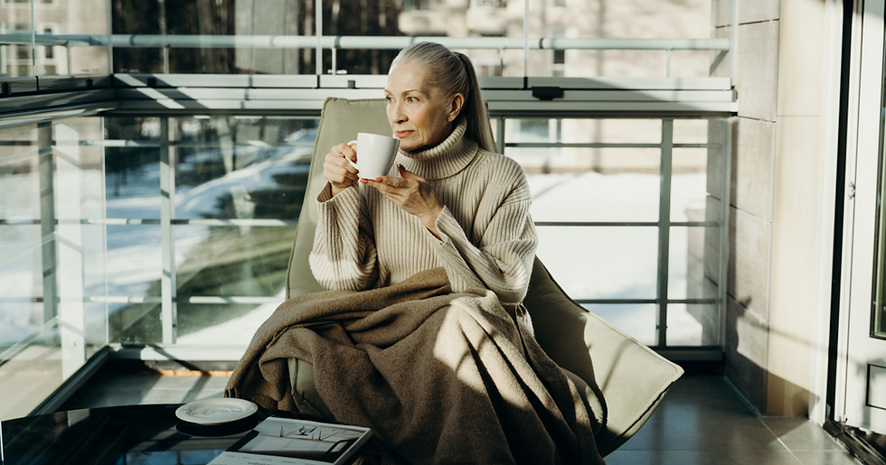 An older lady sitting on a chair drinking a cup of tea