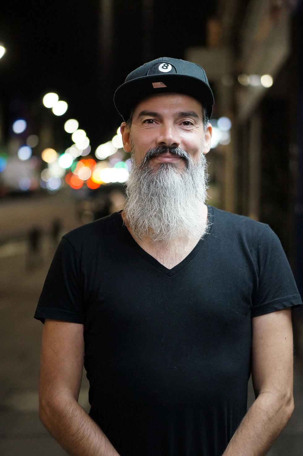 Man with long grey beard, black shirt, and cap at night