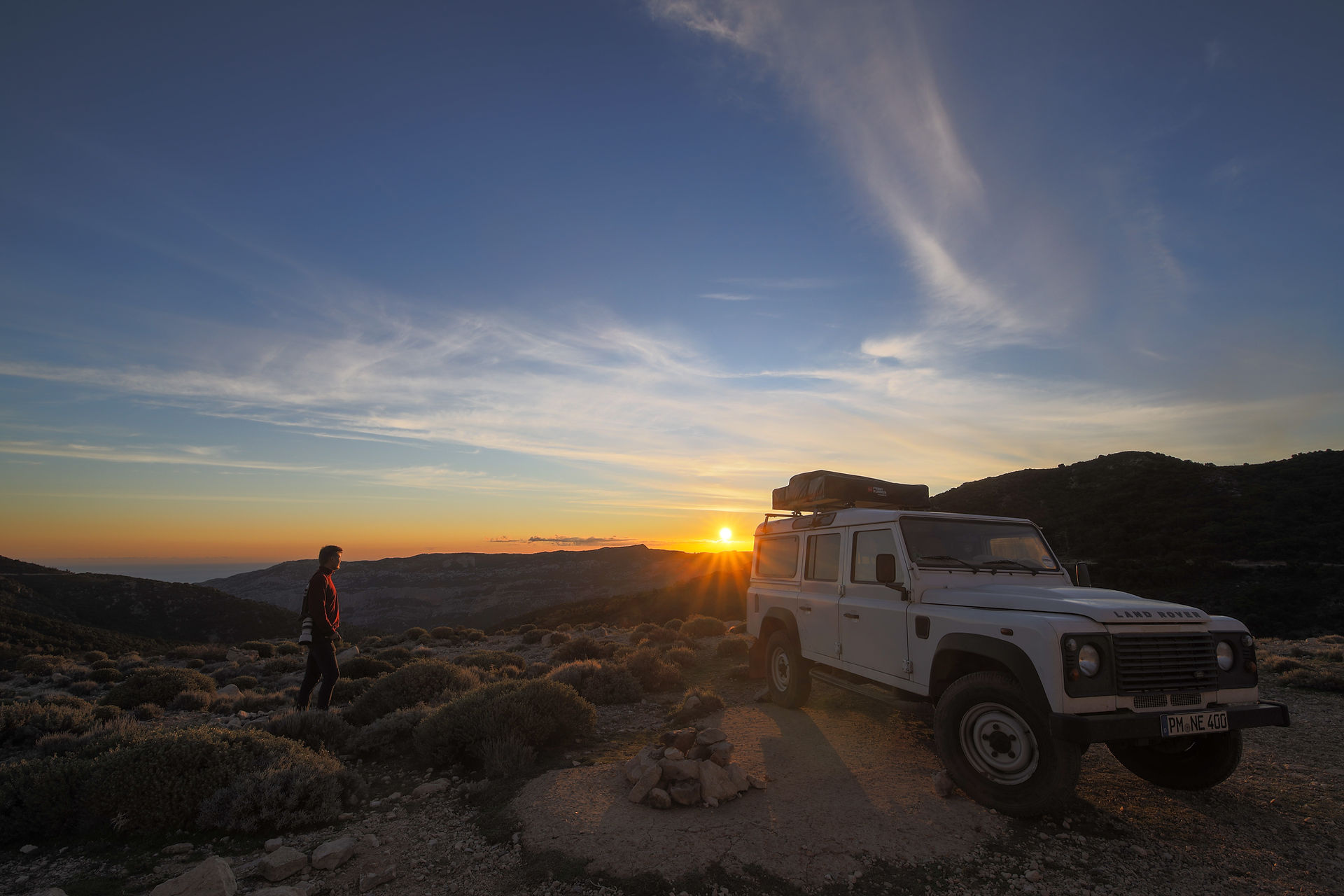 Mann beobachtet Sonnenaufgang in den Bergen in Sardinien mit einem Camper