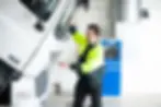 A smiling Truckrite heavy vehicle technician in a hi-vis jacket inspecting the engine bay of a DAF truck in a modern workshop