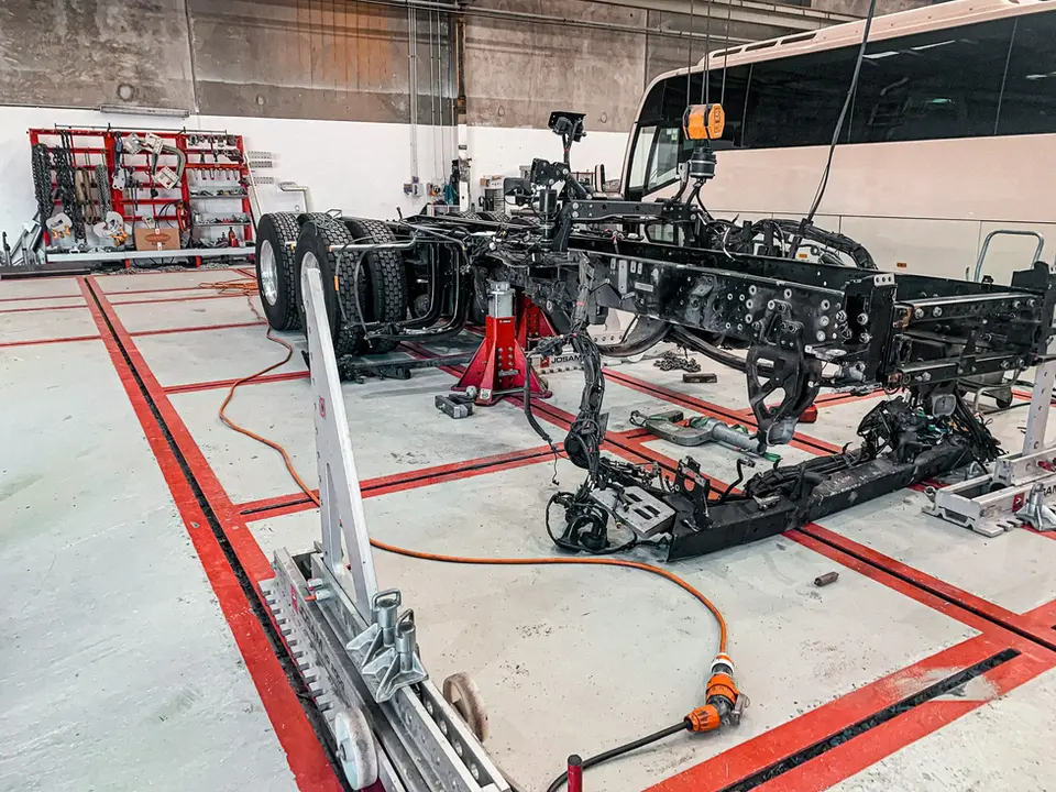 Heavy vehicle chassis on red stands in a dedicated chassis alignment garage surrounded by tools