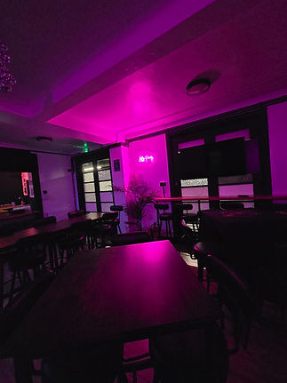 Main seating area in Dorothy's Community Hub. The area is illuminated by light from a neon pink "let's party" decoration that's hanging on the wall.