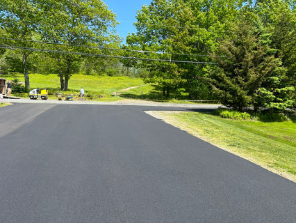Newly paved asphalt driveway with green trees and grass