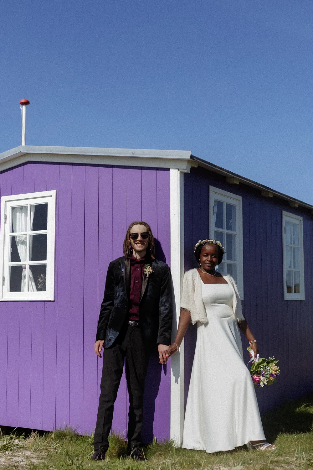 Bride and groom laughing together pink fishing hut the coastline of Ærø island.