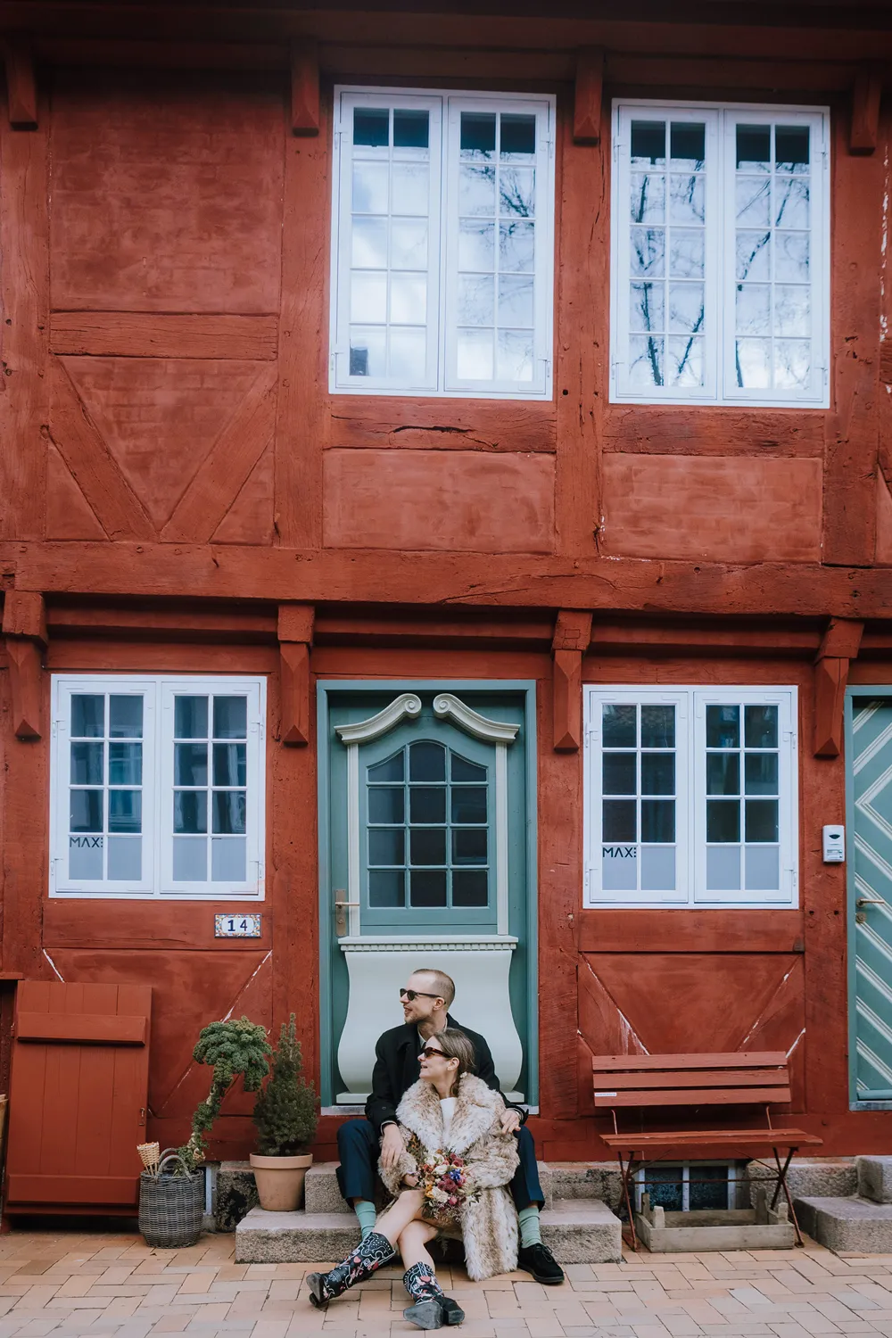 Couple sitting beside colourful historic house in Odense after city hall wedding.