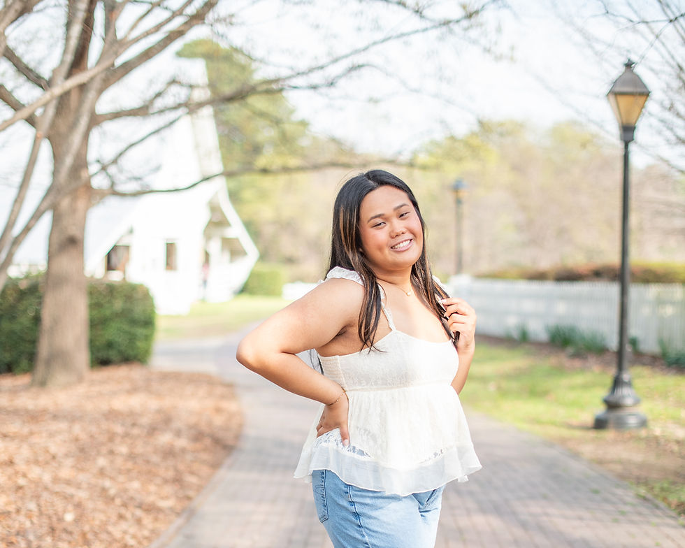 Senior photography session at Historic Oak View County Park in Raleigh, NC in the spring. Girl in white shirt and jeans standing with hand on hip on a paved path.
