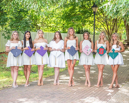 Senior ambassador team wearing white dresses and holding graduation caps at Historic Oak View County Park in Raleigh, NC.