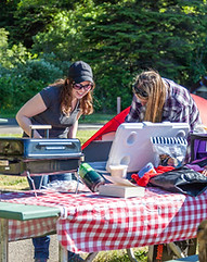 Two smiling women looking in a cooler and setting up a picnic and bbq near their tent at Windy Cove A campground