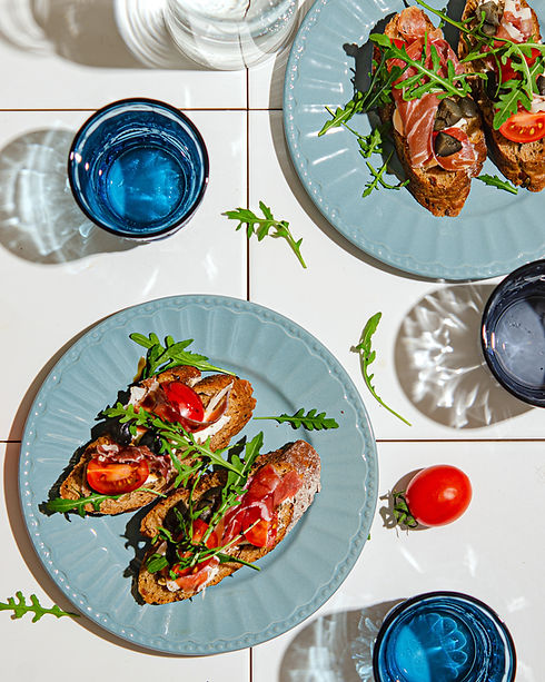 bruschetta-with-dark-baguette-jamon-arugula-tomato-white-tile-table-bright-hard-sunlight-h