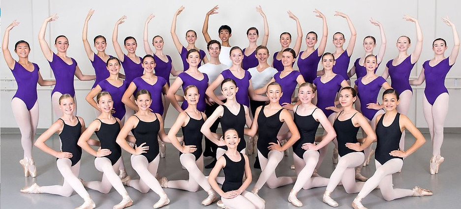 A large group of pre professional ballet students pose elegantly in their advanced training class