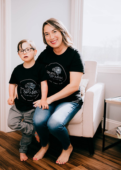 Mother and child wearing matching NeuroSPARK Therapies shirts, smiling and sitting together