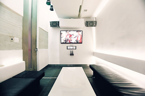 Maru Karaoke Lounge Private Room, Showing karake system, speakers, TV, a table amd seatings in bright white ambient light.
