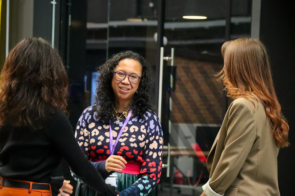 Katie is talking to two females. She is wearing a multicoloured leopardprint jumper and blue glasses