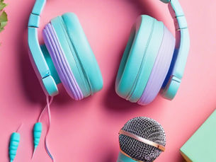 on a pink background there is a set of headphones that lay in the centre of the image. They are teal coloured with purple accents. Additionally, there is the head of a grey microphone at the bottom of the image.