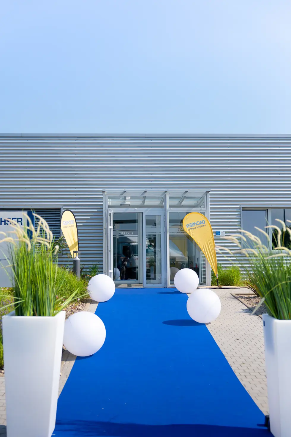 Entrée événementielle Dachser avec tapis bleu, ballons lumineux blancs et oriflammes jaune