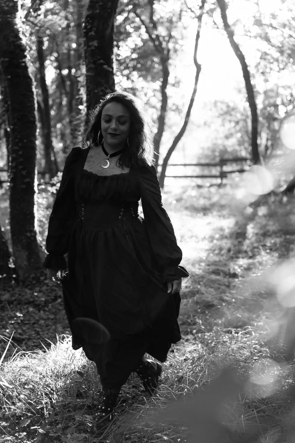 Femme en robe gothique noire marchant dans une forêt ensoleillée, photographie artistique 