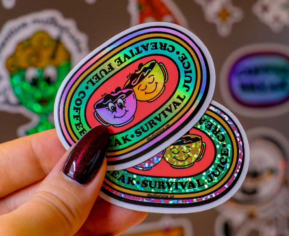 Hand holding holographic oval stickers featuring cartoon coffee cups and the text Creative Fuel, Coffee Break, Survival Juice.