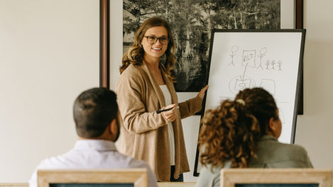 Woman presenting at a whiteboard to seated audience.