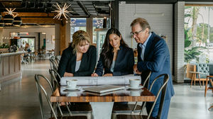 Three people reviewing blueprints at a table.