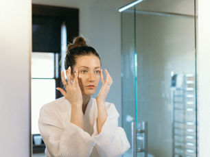 A woman in a bath robe applying hydrating skincare in a bathroom mirror.