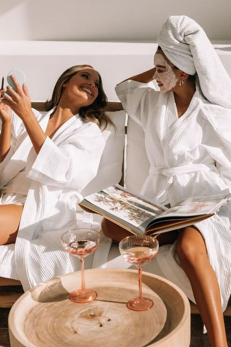 Two girls having a spa day in the sunshine in fluffy robes and one has a skincare mask on.