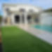 The backyard of a white residential, featuring green synthetic turf and a pool