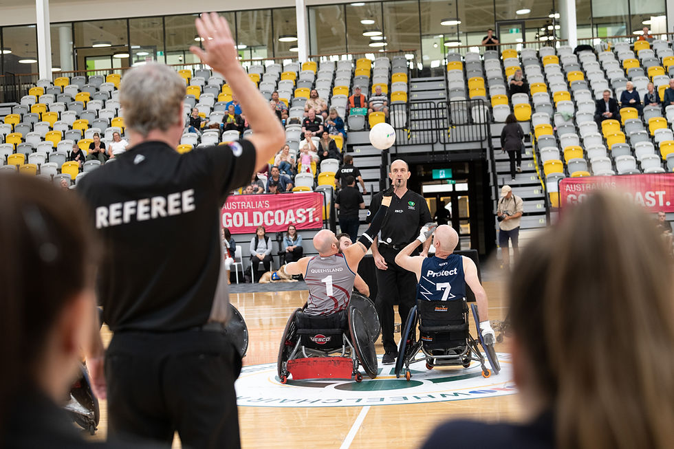 Wheelchair Rugby Nationals. Two players are reaching up to a ball in the air. Standing in front of them is an unpire with a whistle in their mouth.