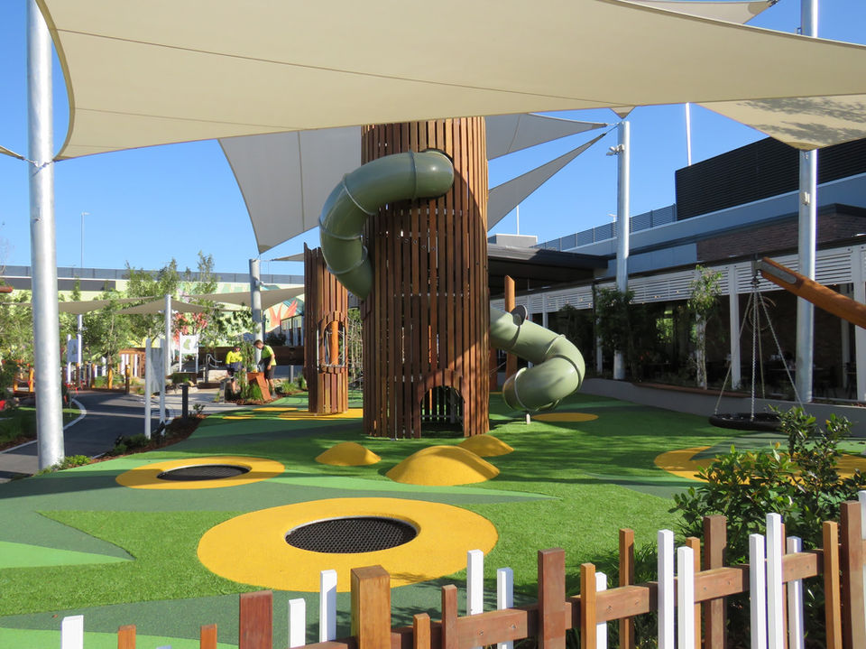 A large playground with a wooden tower and green slide, featuring vibrant green synthetic turf.