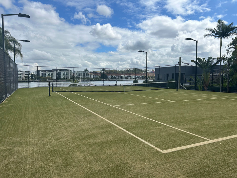 An outdoor tennis court with green synthetic turf used as the surface.