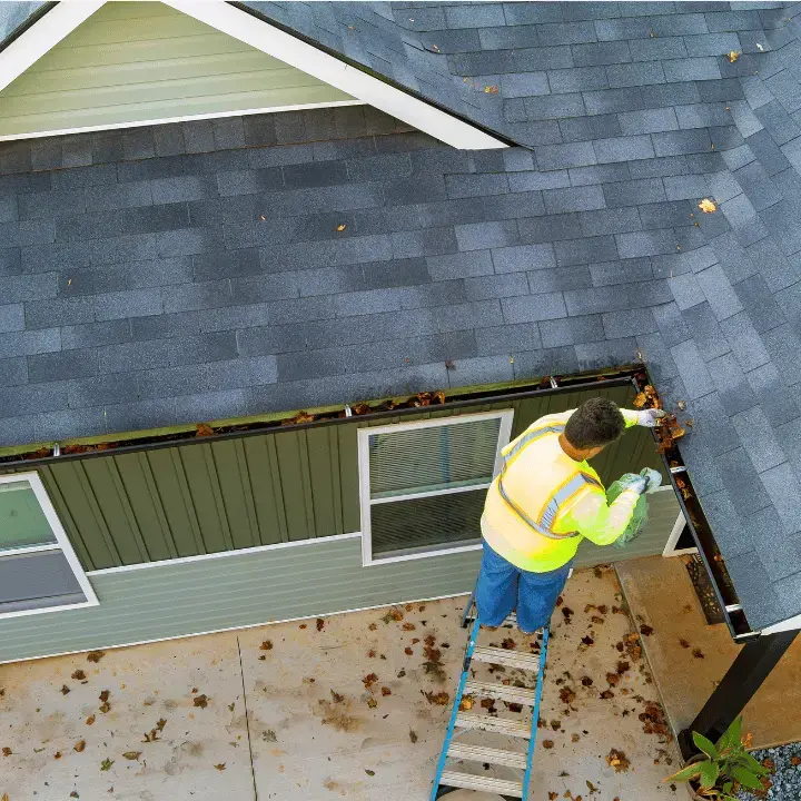 Technician on a ladder cleaning gutters full of leaves in Redmond, Oregon