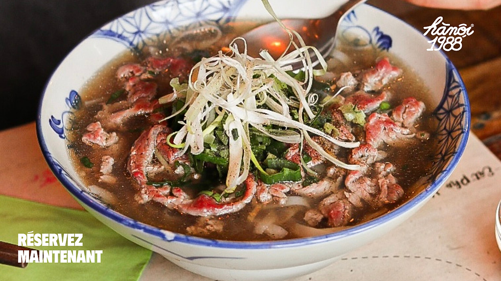 Bowl of beef noodle soup - pho bo - topped with herbs and shredded scallions on a table