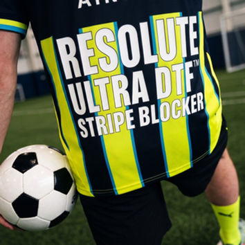football player on indoor turf holds a ball, wearing a black and neon striped jersey with RESOLUTE ULTRA DTF STRIPE BLOCKER.