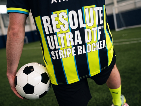 football player on indoor turf holds a ball, wearing a black and neon striped jersey with RESOLUTE ULTRA DTF STRIPE BLOCKER.