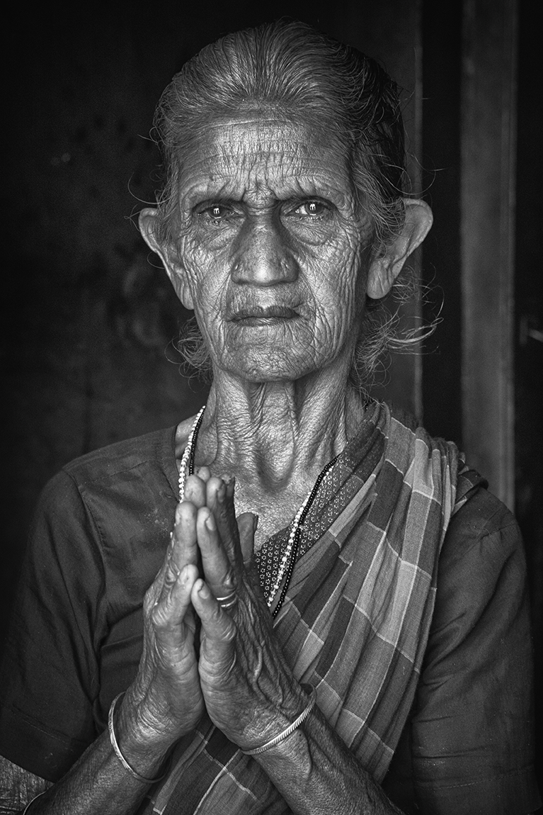 Black and white portrait of an elderly woman with hands clasped in prayer, her expression solemn and serene — a powerful cultural study by Cristian Mitrani.