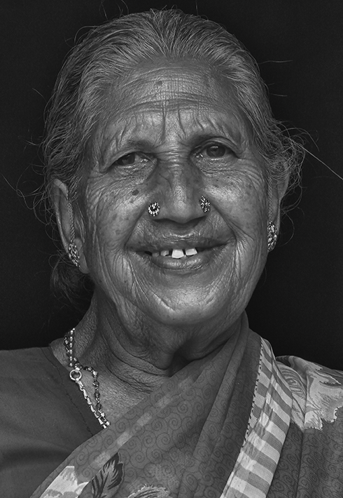 Black and white close-up portrait of a smiling elderly woman wearing traditional jewelry and sari, radiating warmth and wisdom — a heartfelt capture by Cristian Mitrani.
