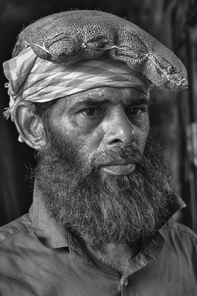 Black and white close-up portrait of a bearded man wearing a textured cloth wrapped on his head, with a contemplative expression — a detailed cultural study by Cristian Mitrani.