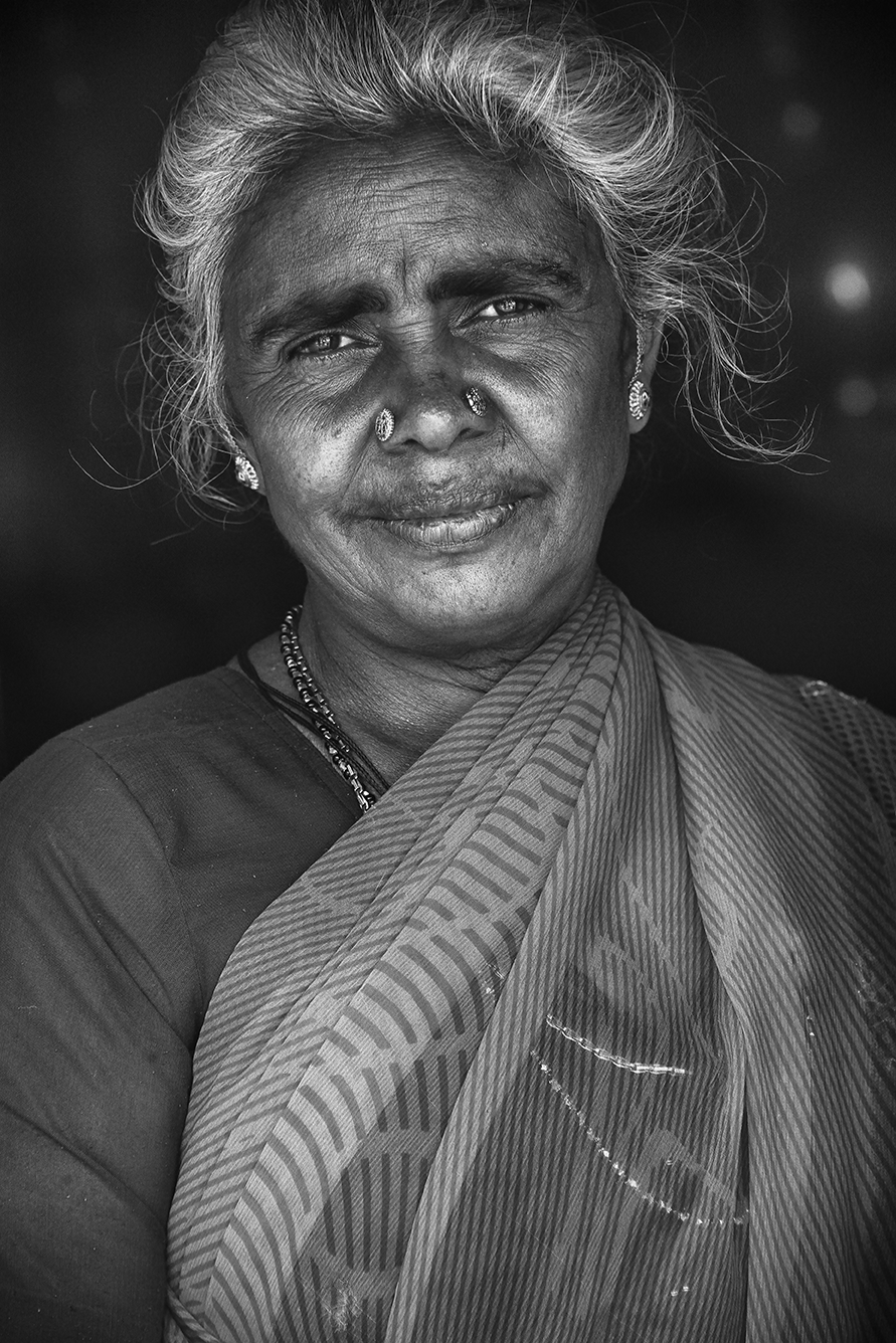 Black and white portrait of an elderly woman wearing a sari, smiling gently with soft lighting enhancing her features — an intimate and dignified moment by Cristian Mitrani.