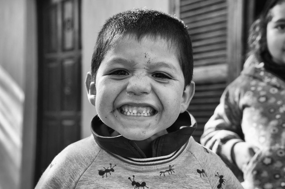 Black and white close-up of a joyful young boy grinning widely, his face full of playful energy — a candid moment by Cristian Mitrani.