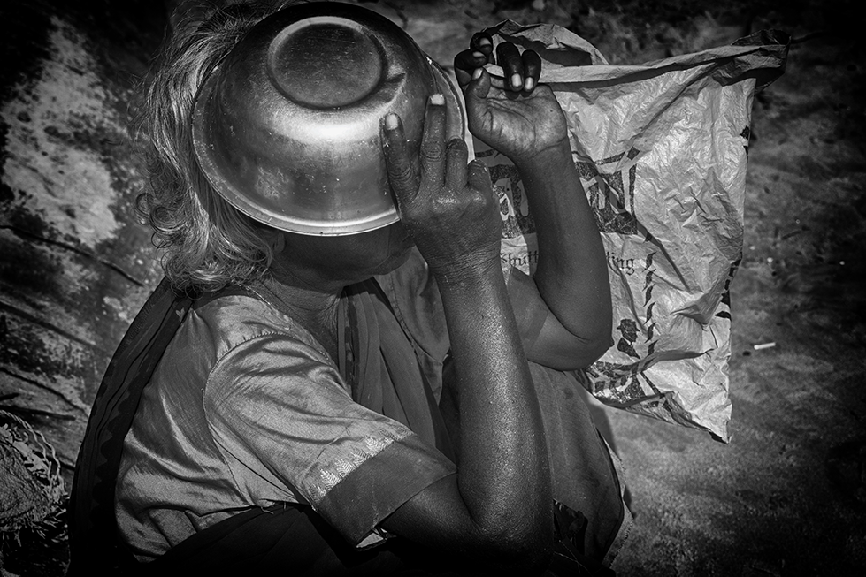 Black and white photo of a person shielding their face with a metal bowl, highlighting themes of hardship and resilience — a raw and poignant capture by Cristian Mitrani.