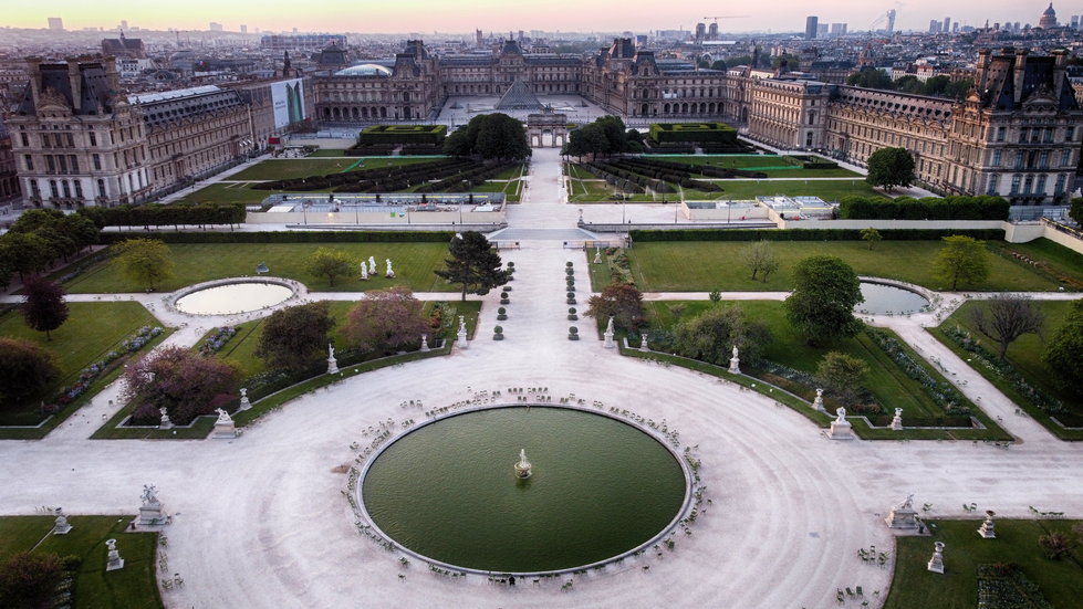 An overhead photograph by Cristian Mitrani showcasing the expansive Tuileries Garden in Paris. The image features symmetrical pathways, manicured lawns, and rectangular flowerbeds leading toward the historic Louvre Palace in the background. The central circular fountain is prominently displayed in the foreground, capturing Mitrani's detailed and textured photographic style.