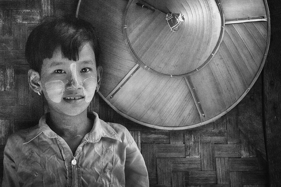 Black and white portrait of a young child smiling beside a large umbrella, captured with soft light — a tender moment by Cristian Mitrani.