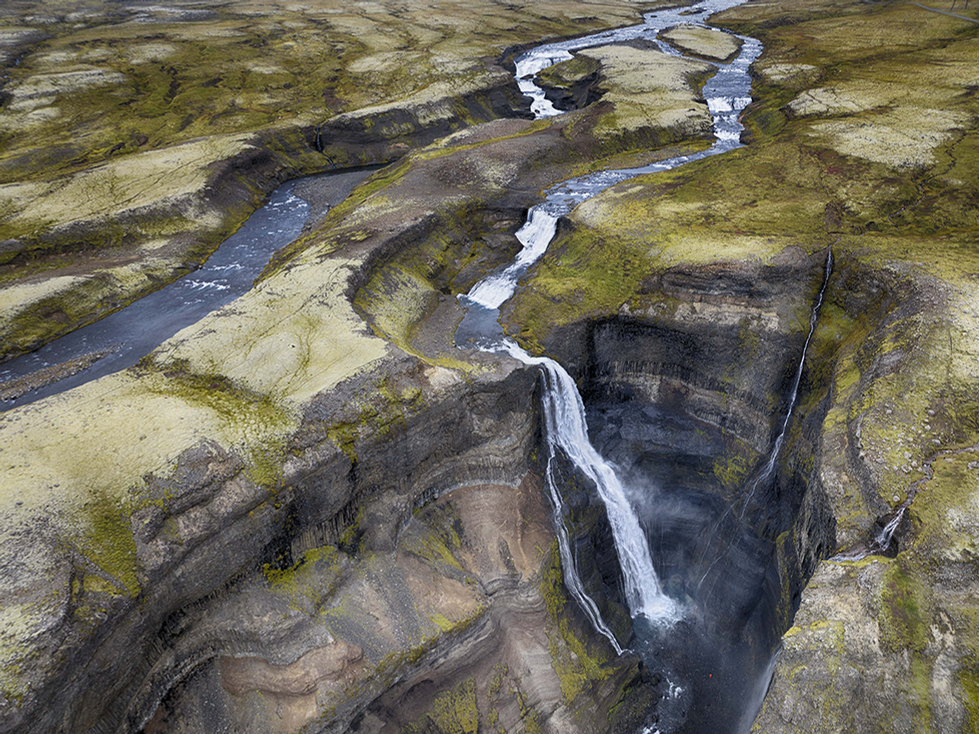 A stunning aerial view of a cascading waterfall flowing through a rugged, moss-covered landscape with winding streams. This natural scene exemplifies Cristian Mitrani's appreciation for capturing the dynamic beauty and raw power of nature's landscapes.