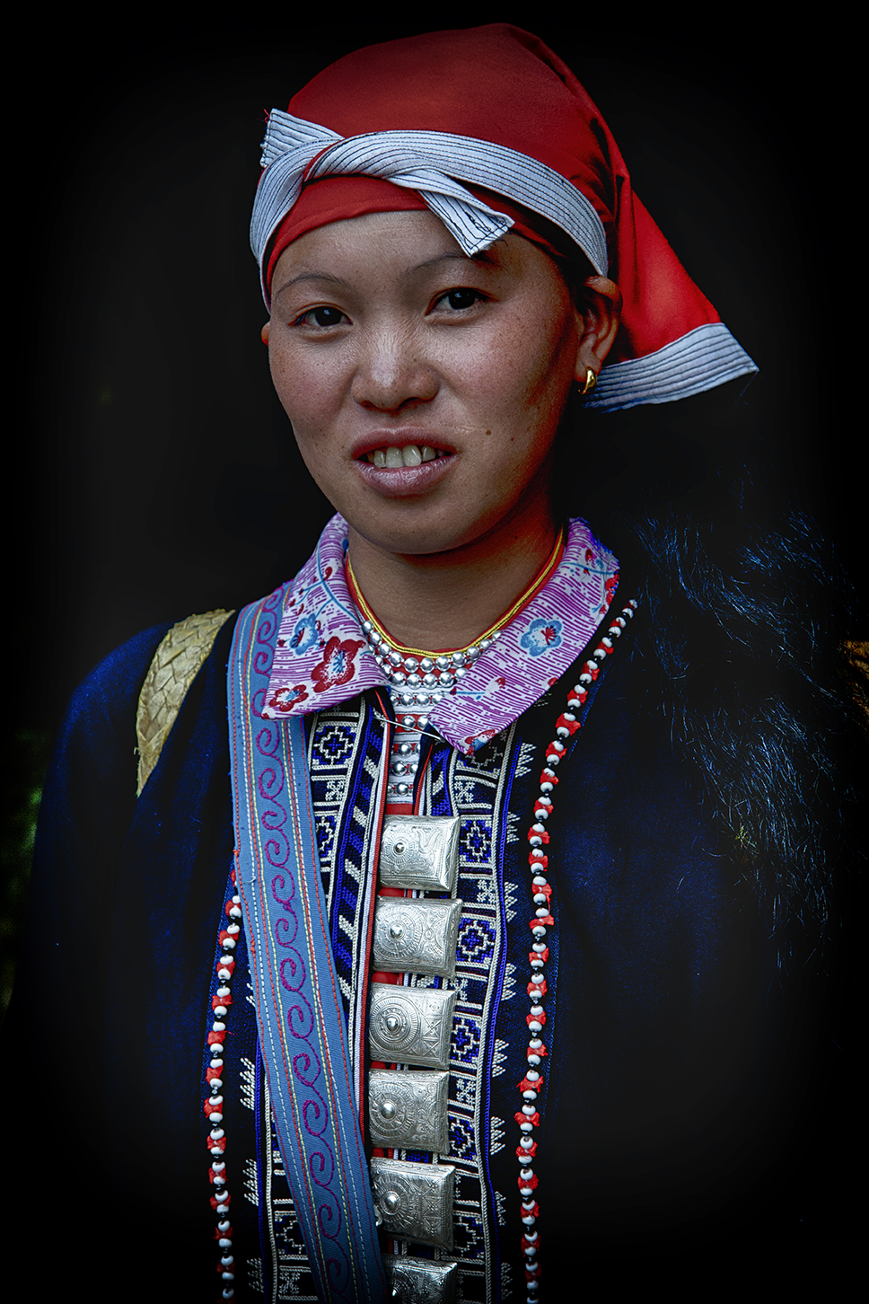 Portrait of a young woman dressed in vibrant traditional attire, smiling warmly against a dark background — a colorful cultural capture by Cristian Mitrani.