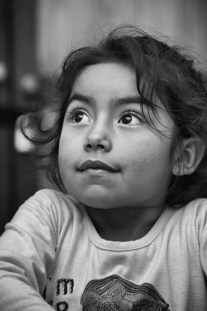 Black and white close-up of a thoughtful young girl gazing upward with soft expression — a tender portrait by Cristian Mitrani.