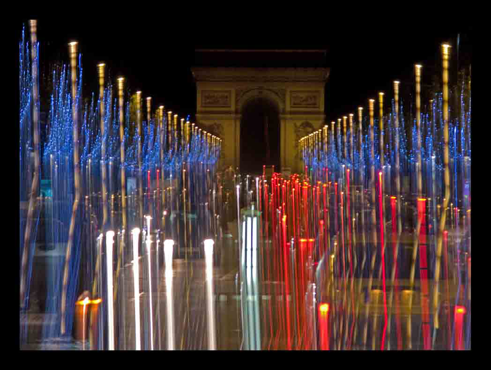 Long-exposure photograph of the Arc de Triomphe with vibrant red, blue, and white light trails on the Champs-Élysées — a dynamic Parisian nightscape by Cristian Mitrani.