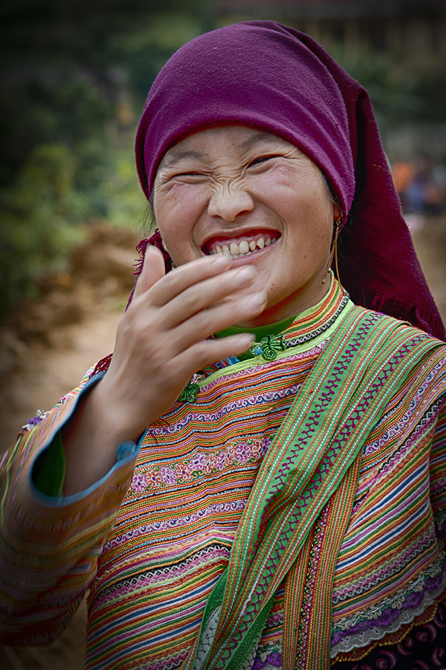Smiling young woman wearing colorful traditional dress and headscarf, expressing happiness — a lively cultural photo by Cristian Mitrani.